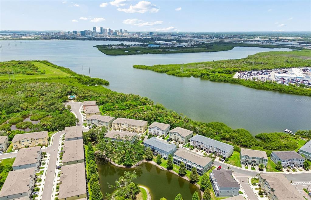 An aerial view shows a residential complex with a pond, surrounded by greenery and water — 4755 TUSCAN LOON DRIVE, TAMPA, FL