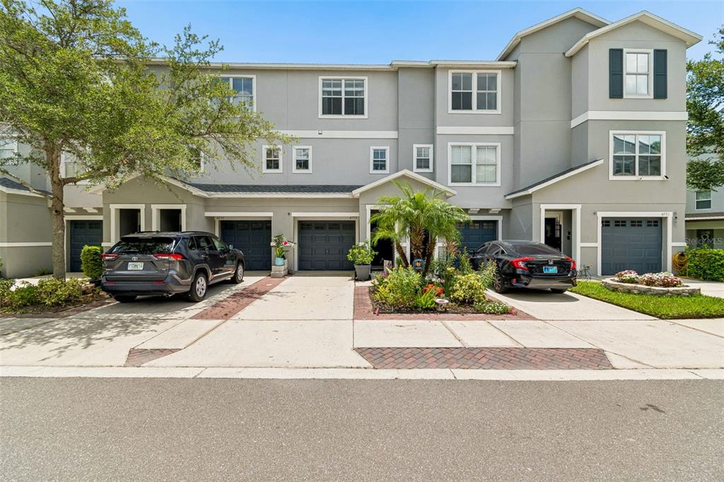 A multi-story townhouse exterior with two garages, two parked cars, and a landscaped front yard — 4755 TUSCAN LOON DRIVE, TAMPA, FL