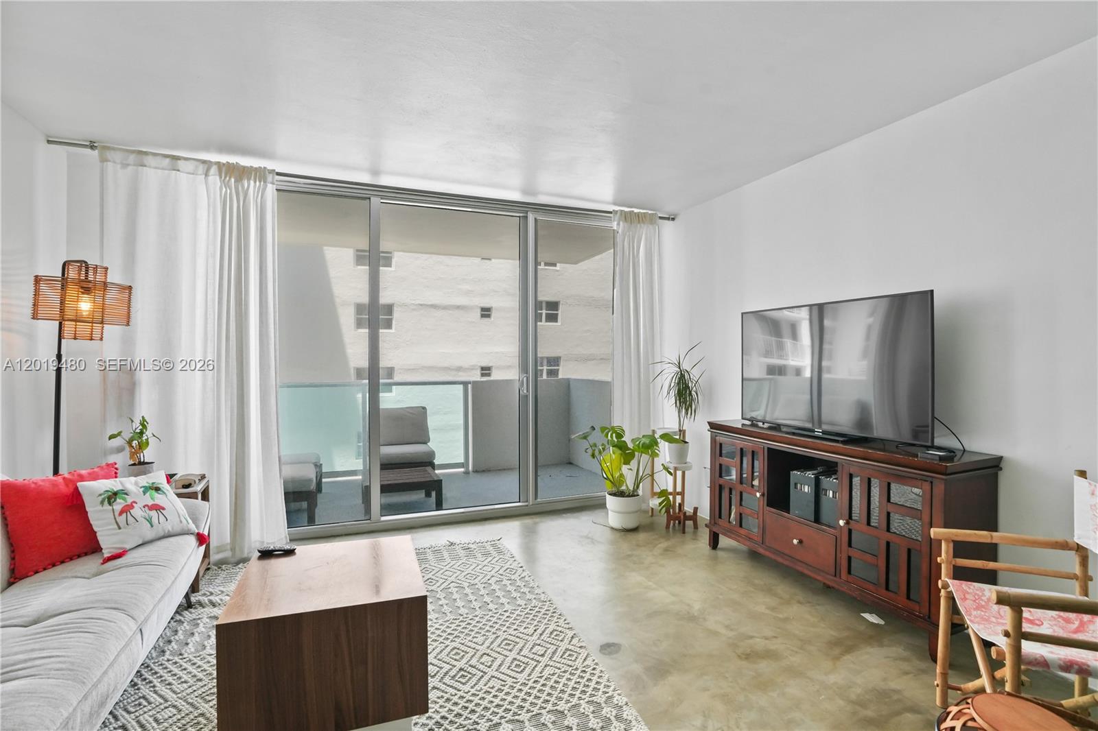 A living room features a sofa, television console, concrete floors, and a sliding glass balcony door — 1200 West Ave # 819, Miami Beach FL 33139, MIAMI BEACH, FL