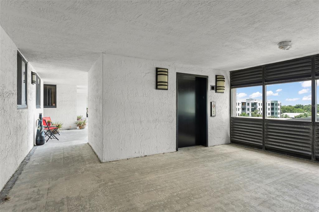 A concrete-floored elevator lobby features white textured walls, a black door, and slatted exterior windows — 530 E CENTRAL BOULEVARD UNIT 503, ORLANDO, FL