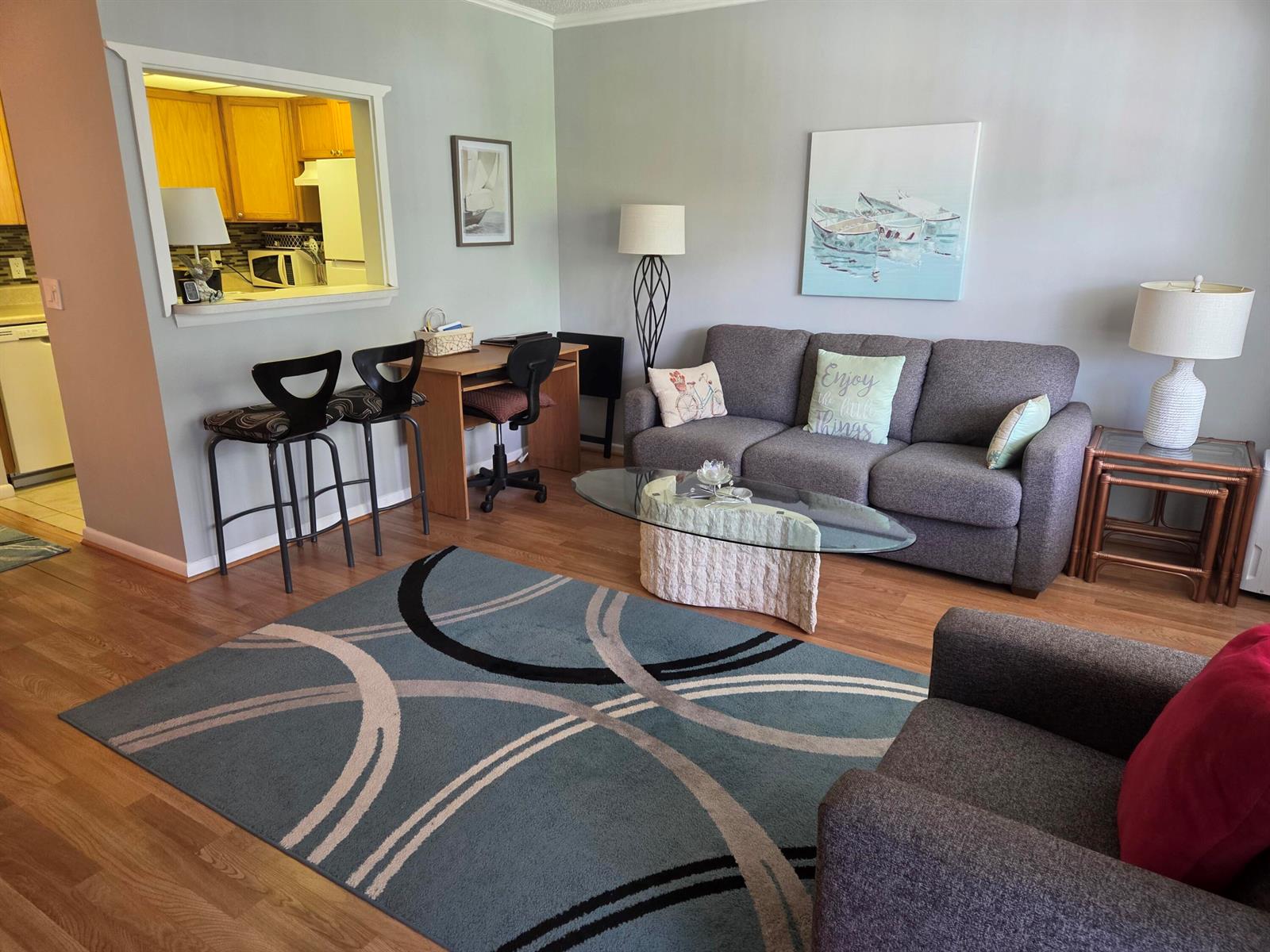 A living room with a gray sofa, area rug, coffee table, and a kitchen pass-through — 138 Newport I, Deerfield Beach FL 33442, DEERFIELD BEACH, FL