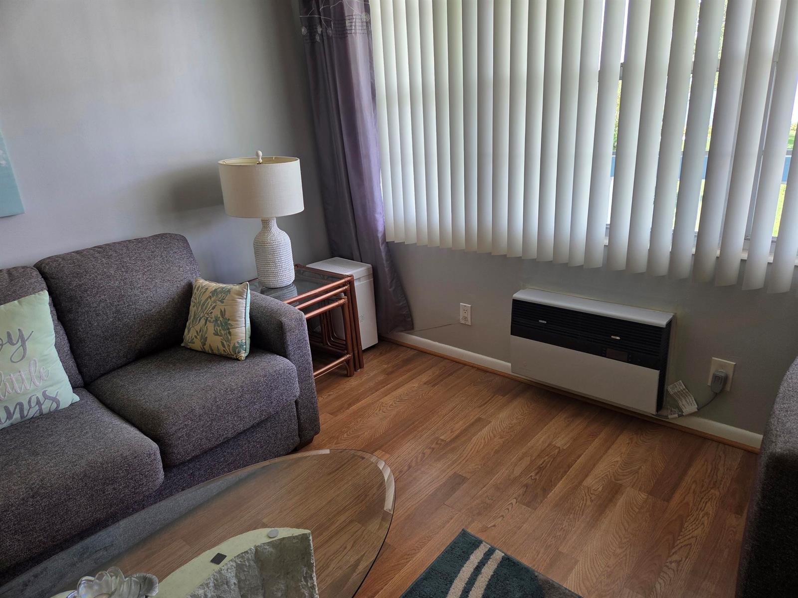 A living room features a gray sofa, a glass-topped side table, and a wall-mounted heater — 138 Newport I, Deerfield Beach FL 33442, DEERFIELD BEACH, FL