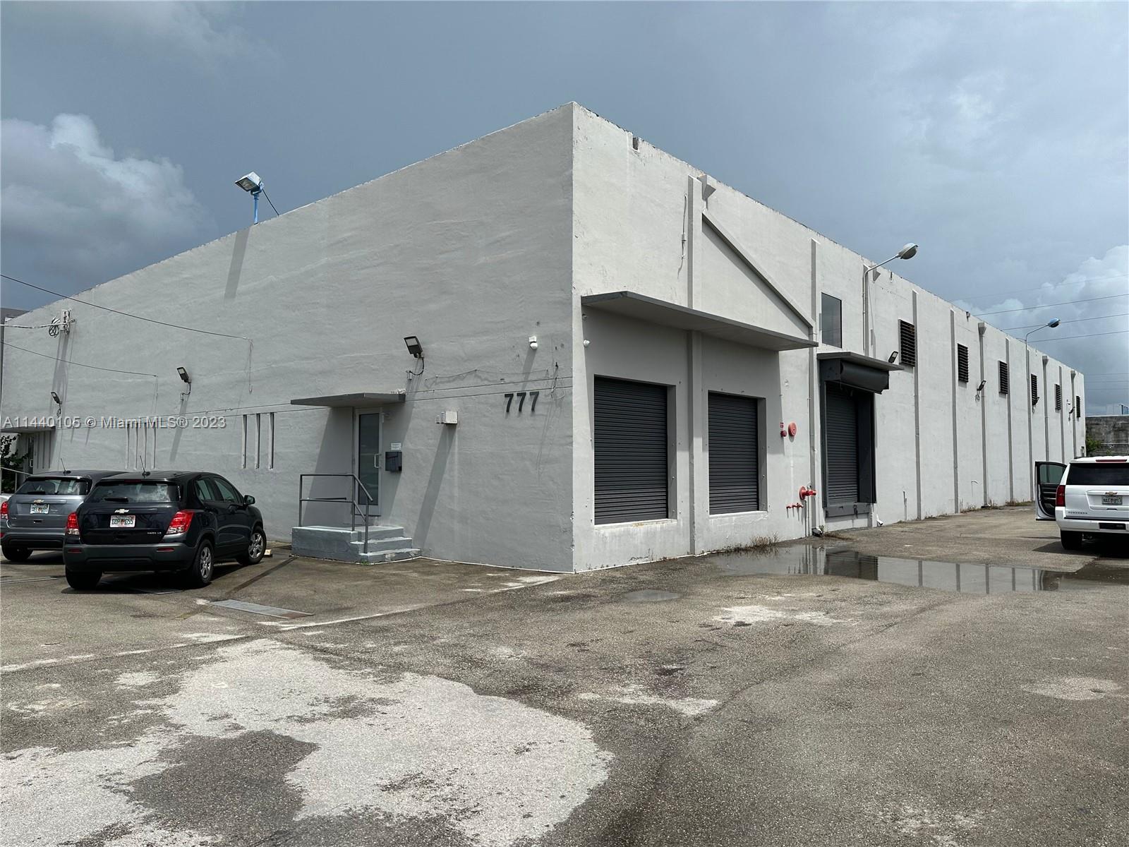 A gray industrial warehouse building features multiple roll-up doors and a small pedestrian entrance — 775 NW 71st St, Miami FL 33150, MIAMI, FL