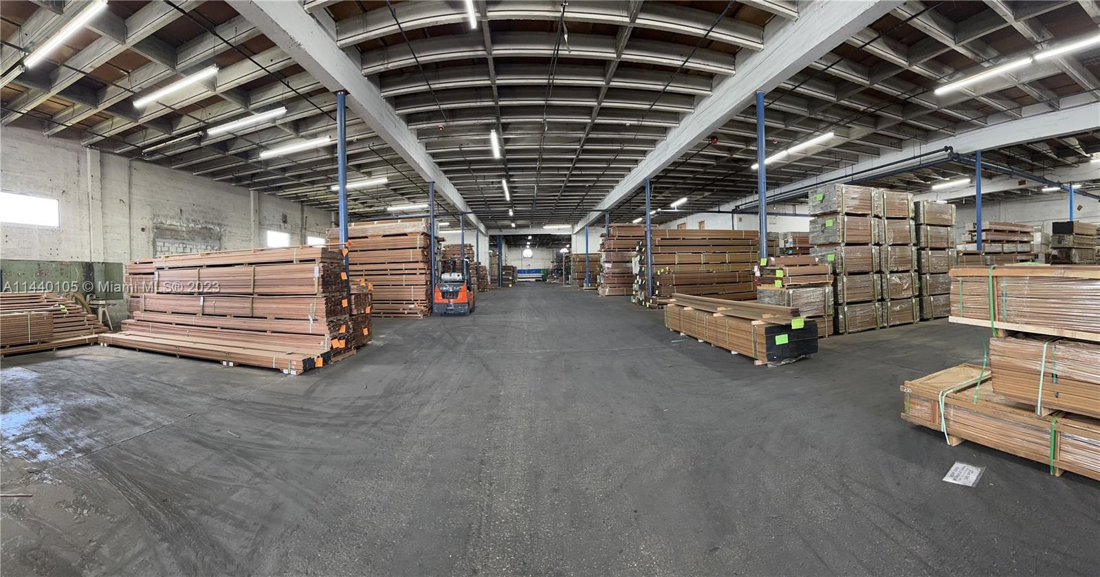 A large industrial warehouse interior features high ceilings and stacks of lumber on pallets — 775 NW 71st St, Miami FL 33150, MIAMI, FL