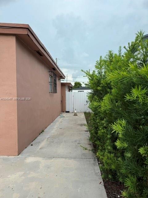 A concrete walkway runs between a peach-colored exterior wall and a tall green hedge — 397 W 57th St # 3, Hialeah FL 33012, HIALEAH, FL
