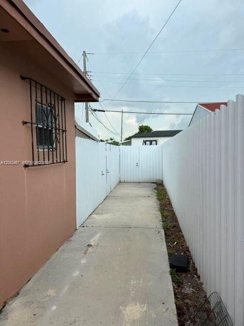 A concrete walkway runs between a peach-colored house wall and a white vinyl fence — 397 W 57th St # 3, Hialeah FL 33012, HIALEAH, FL