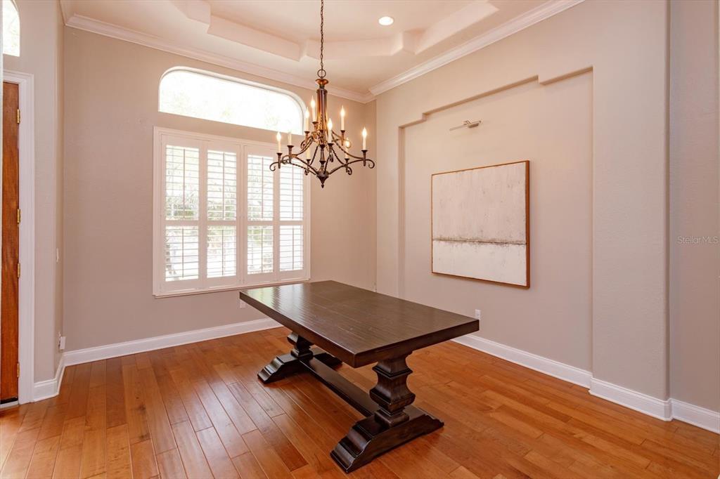 A dining room features a dark wood trestle table, a chandelier, and plantation shutters — 8816 GREAT COVE DRIVE, ORLANDO, FL