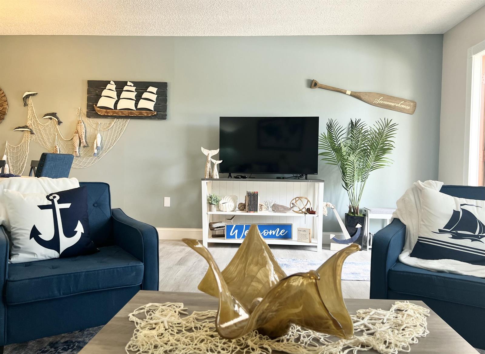 A coastal-themed living room features blue armchairs, a television on a console, and nautical decor — 2600 S Kanner Highway # A4, Stuart FL 34994, STUART, FL