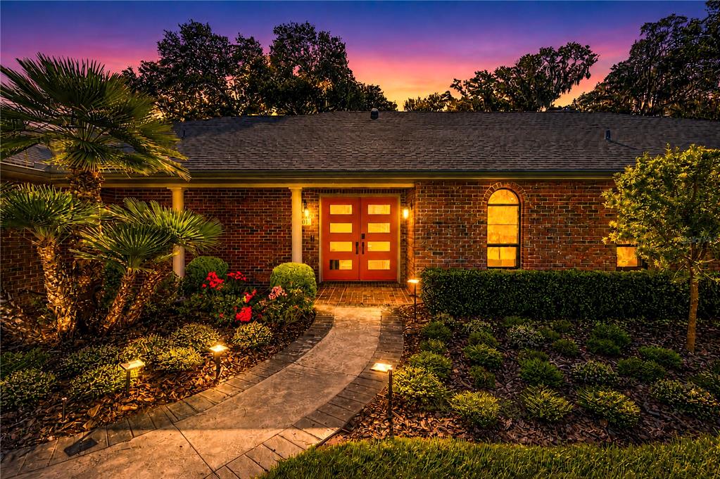 A brick house exterior features a red double front door and a stone walkway at dusk — 5101 NW 80TH AVENUE ROAD, OCALA, FL