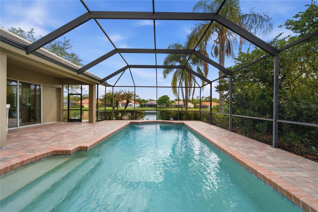 A screened-in swimming pool with a brick paver deck overlooks a lake and houses — 17210 BROADOAK DRIVE, TAMPA, FL