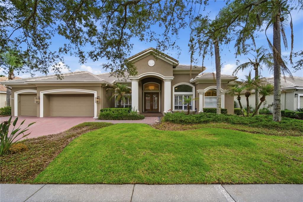 A tan single-story house with a three-car garage, arched entryway, and a manicured front lawn — 17210 BROADOAK DRIVE, TAMPA, FL