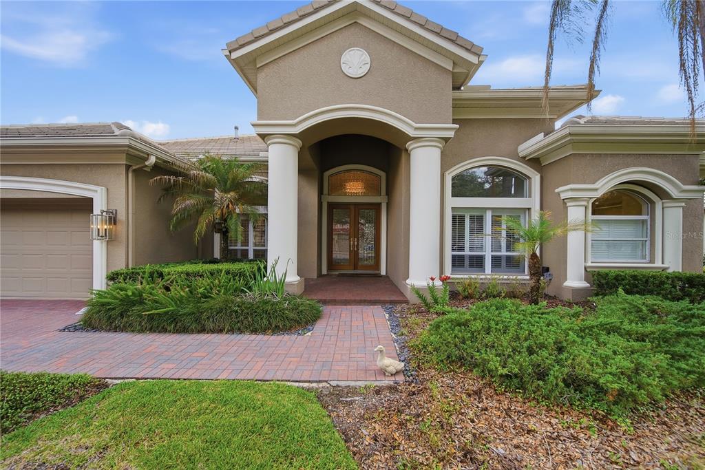 A tan house exterior features a covered entryway with two white columns and a brick walkway — 17210 BROADOAK DRIVE, TAMPA, FL