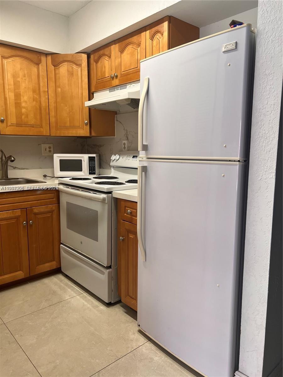 A kitchen features wooden cabinets, a white refrigerator, a stove, and a microwave — 5201 NW 7th St # 314, Miami FL 33126, MIAMI, FL