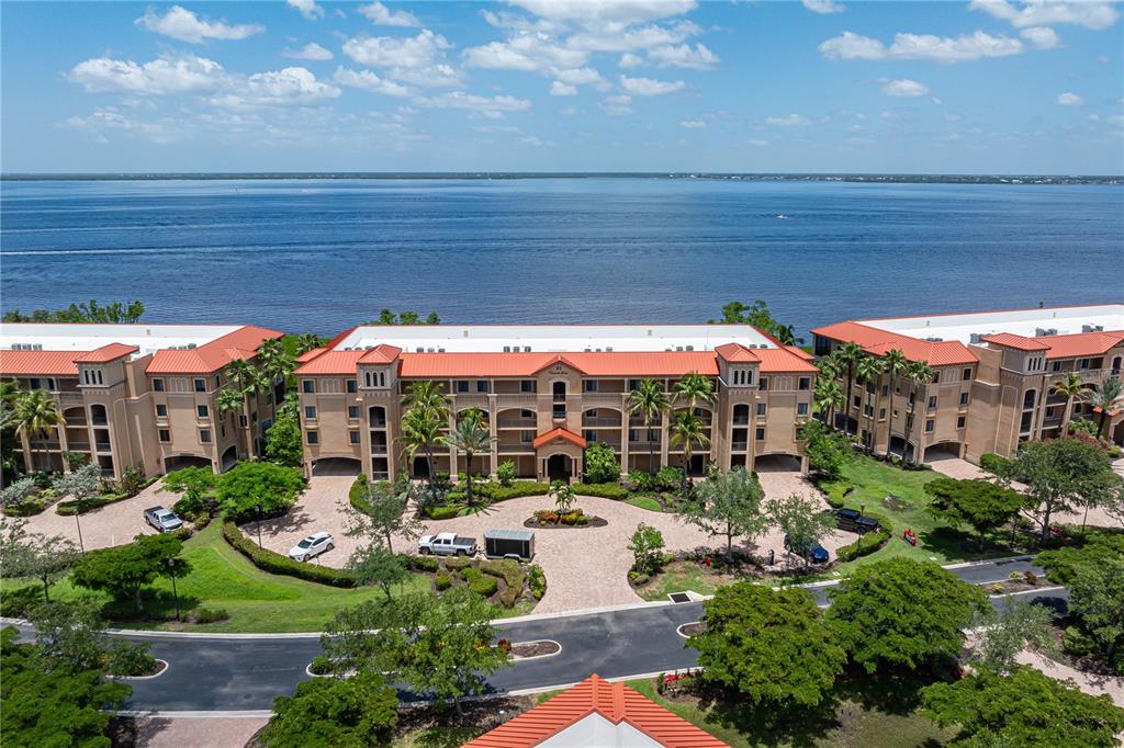 An aerial view of a multi-story waterfront apartment complex with a paved circular driveway — 89 VIVANTE BOULEVARD UNIT 8942, PUNTA GORDA, FL