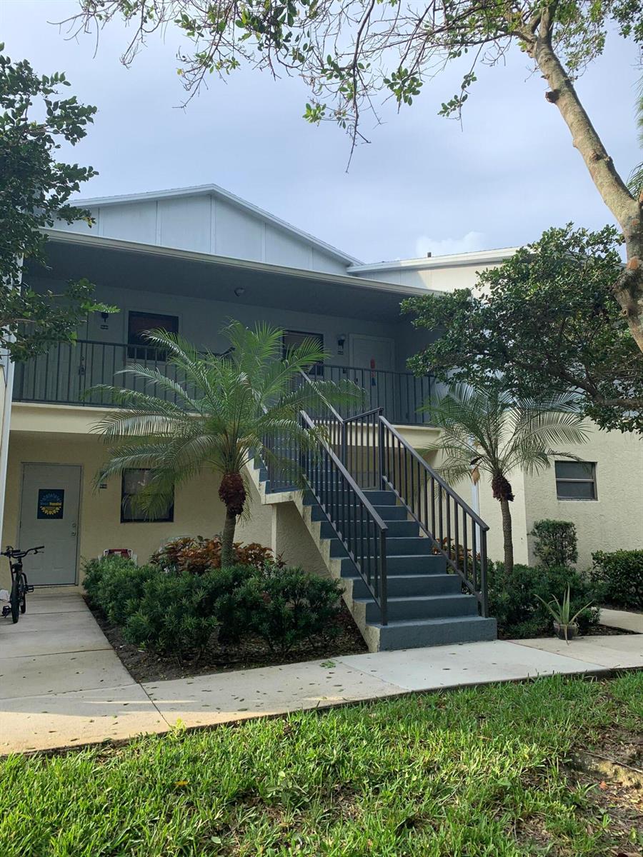 A two-story apartment building exterior features a central staircase, palm trees, and a grassy lawn — 6553 SE Federal Highway # 203, Stuart FL 34997, STUART, FL