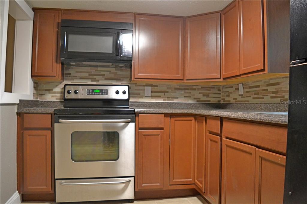 A kitchen features wood cabinets, stainless steel appliances, a dark countertop, and a tiled backsplash — 647 S DELAWARE AVENUE, DELAND, FL