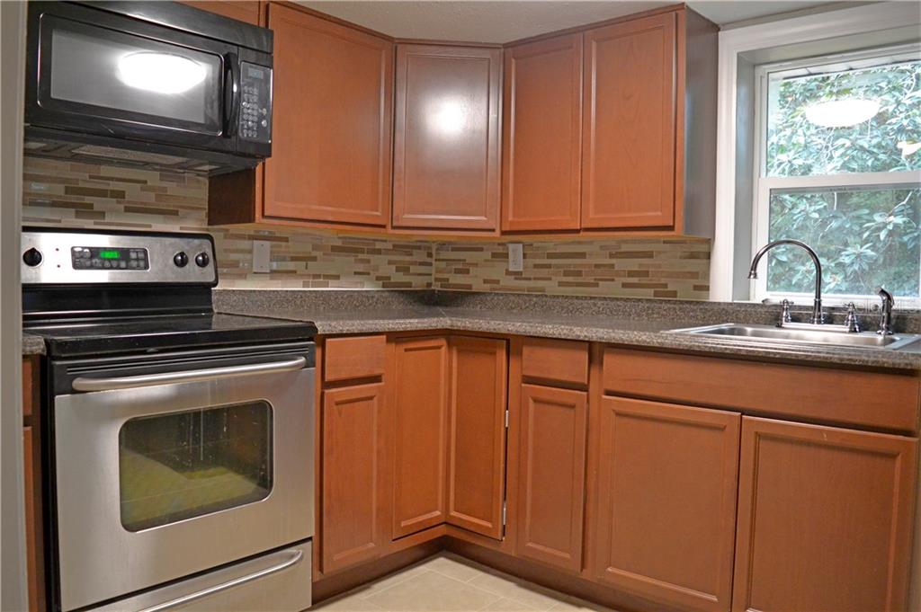 A kitchen features wood cabinets, stainless steel appliances, a tiled backsplash, and a corner sink — 647 S DELAWARE AVENUE, DELAND, FL