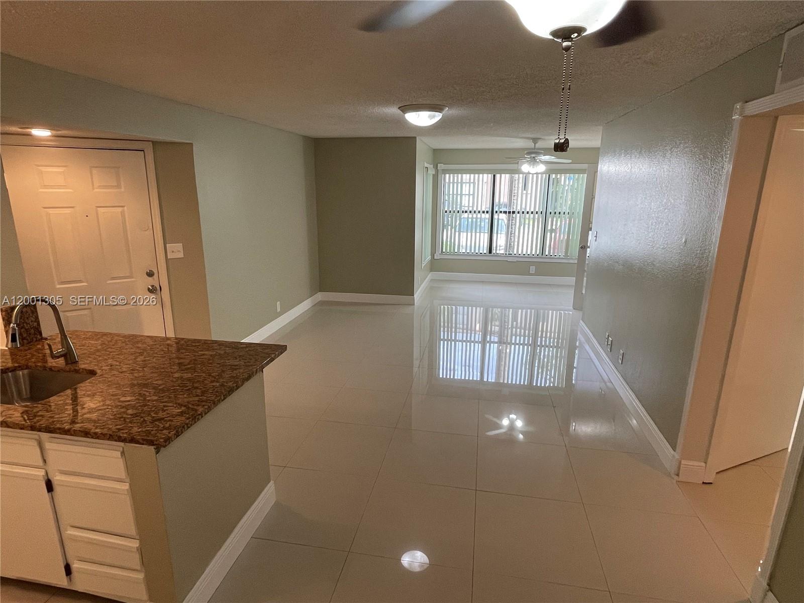 An open-concept living area features light-colored tile flooring, sage green walls, and a granite-topped kitchen island — 2826 S University Dr # 3101, Davie FL 33328, DAVIE, FL