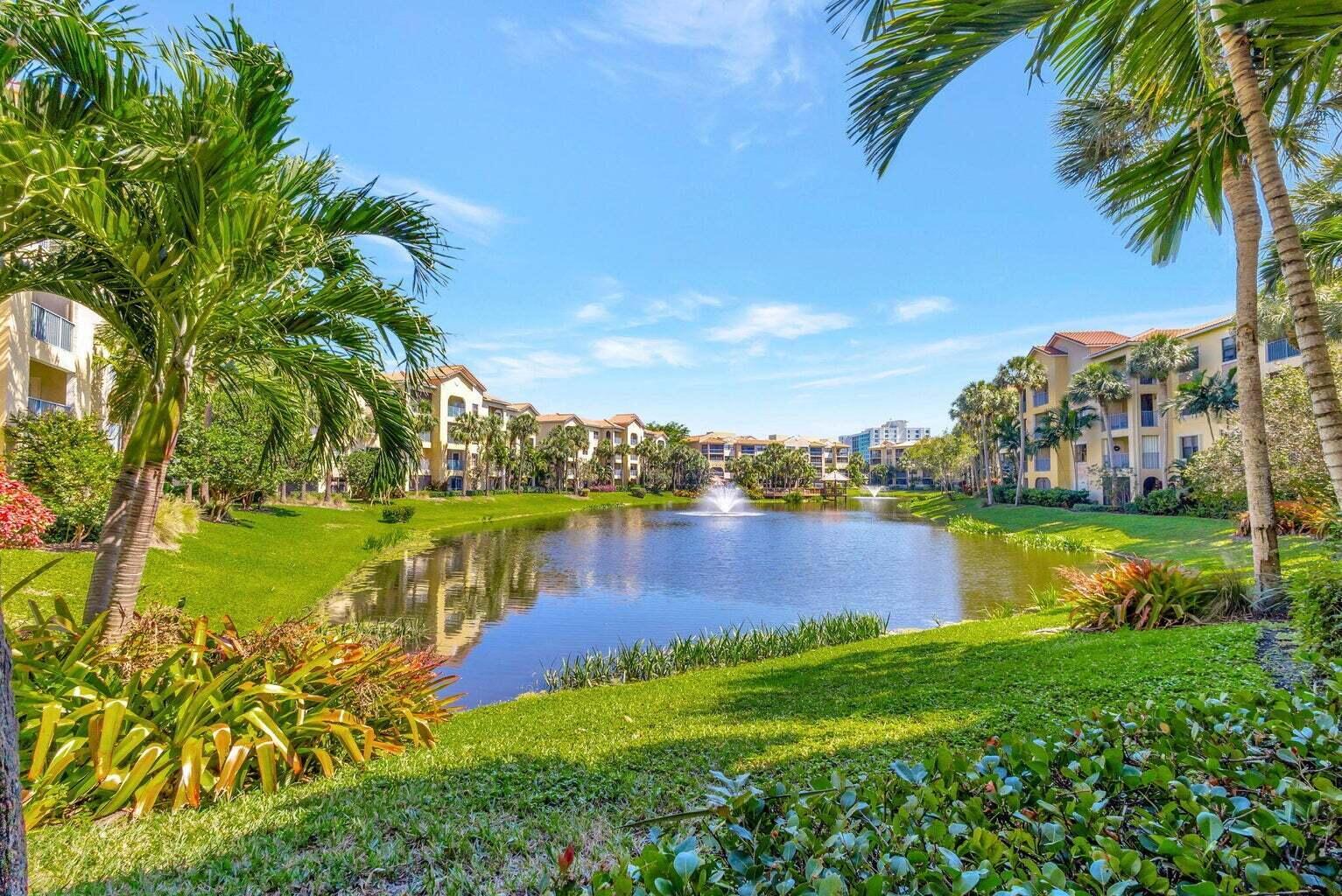 A pond with a fountain sits between multi-story apartment buildings surrounded by palm trees and grass — 300 Uno Lago Drive # 101, Juno Beach FL 33408, JUNO BEACH, FL