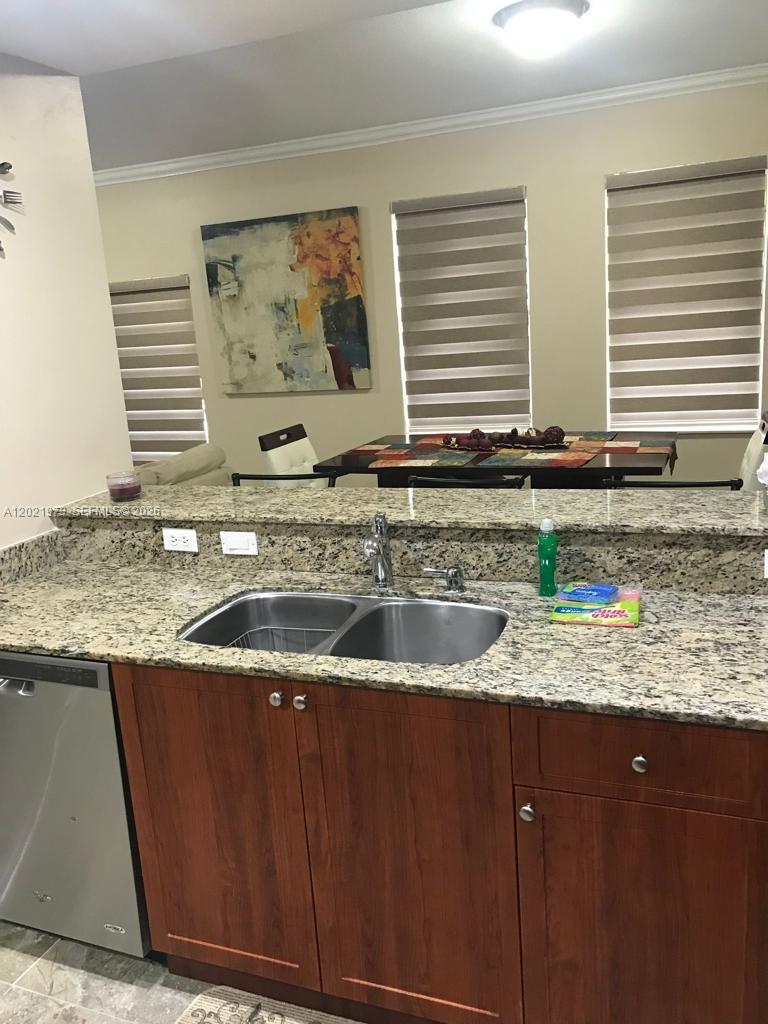 A kitchen features a granite countertop, double sink, and wooden cabinets facing a dining area — 10850 NW 89th Ter # 5, Doral FL 33178, DORAL, FL