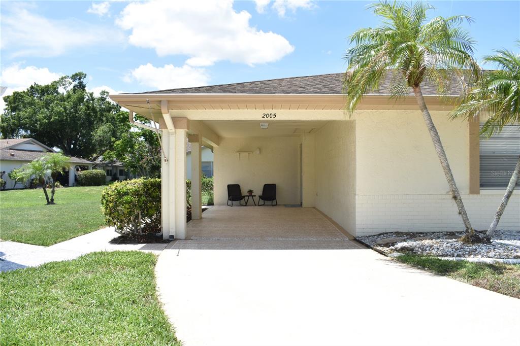 A covered carport with a concrete floor and two chairs sits in front of a house — 2005 HALMROCK PLACE UNIT 174, SUN CITY CENTER, FL