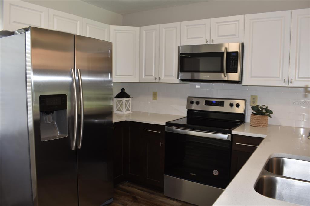 A kitchen features white upper cabinets, dark lower cabinets, stainless steel appliances, and white countertops — 2005 HALMROCK PLACE UNIT 174, SUN CITY CENTER, FL