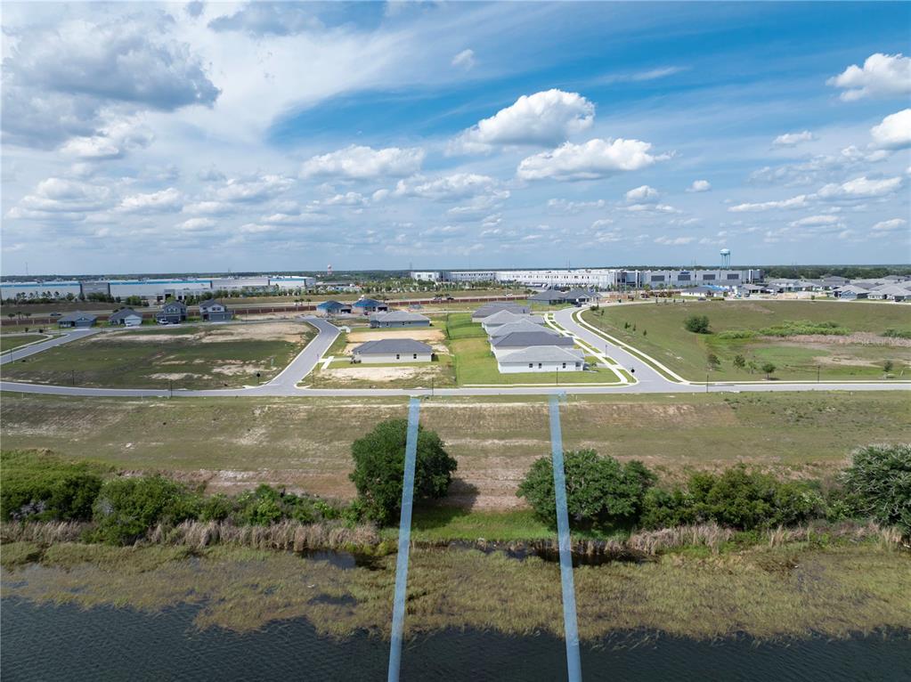 An aerial view shows a residential neighborhood with new houses near a lake and warehouses — 4359 JULIANA LAKE DRIVE, AUBURNDALE, FL