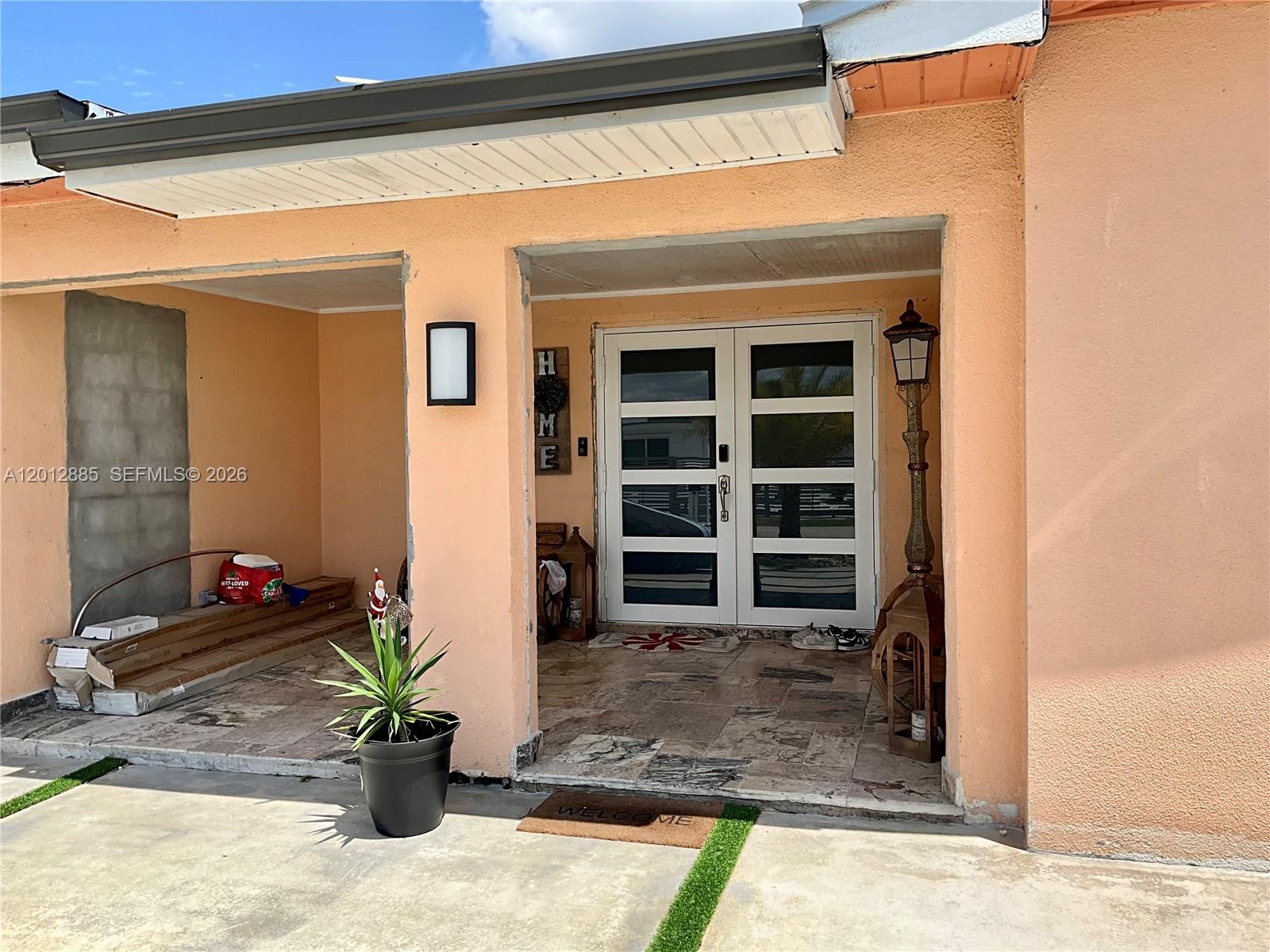 A peach-colored house exterior features a covered entryway with double glass doors and stone flooring — 11251 SW 181st St, Miami FL 33157, MIAMI, FL