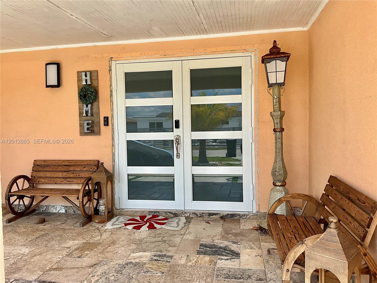 A covered porch features double glass doors, two wooden wagon-wheel benches, and a decorative lamp — 11251 SW 181st St, Miami FL 33157, MIAMI, FL