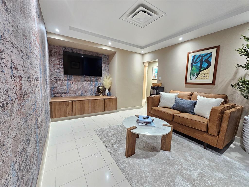 A living room features a wall-mounted television, wood cabinetry, a leather sofa, and tiled floors — calle 8 JOSE PADILLA EL CARIBE, CIDRA, PR