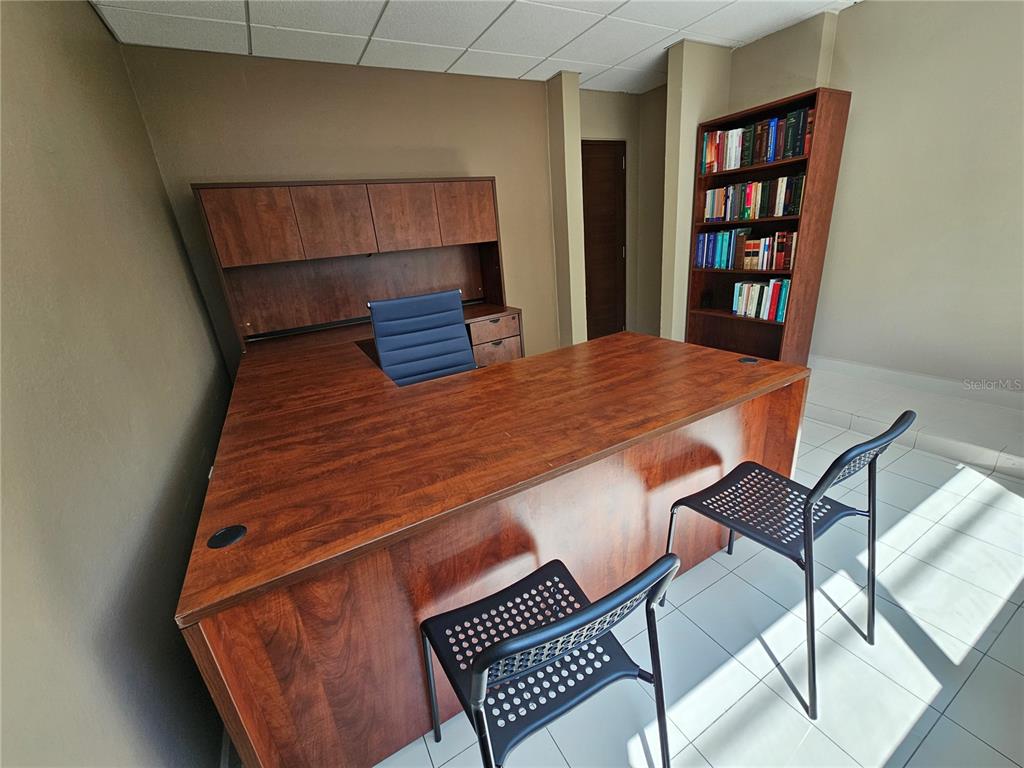 An office features a wooden desk with a hutch, a bookshelf, and two black chairs — calle 8 JOSE PADILLA EL CARIBE, CIDRA, PR