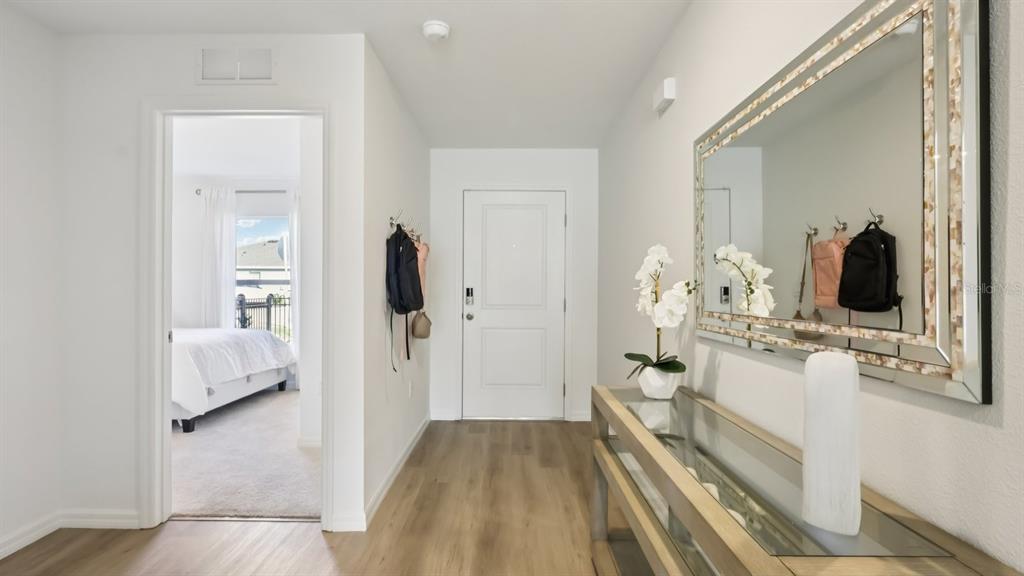 A bright entryway features wood-look flooring, a console table with a mirror, and a doorway — 18708 DRIFTING ELM STREET, SPRING HILL, FL