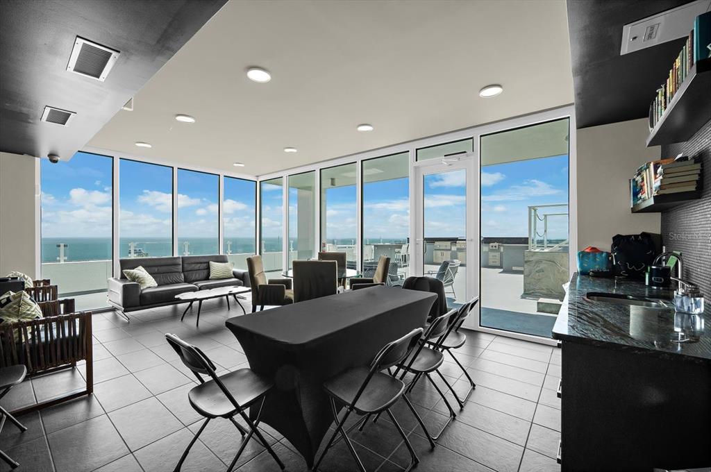 A modern lounge with floor-to-ceiling windows, tile flooring, a dining table, and ocean views — 176 4TH AVENUE NE UNIT 201, ST PETERSBURG, FL