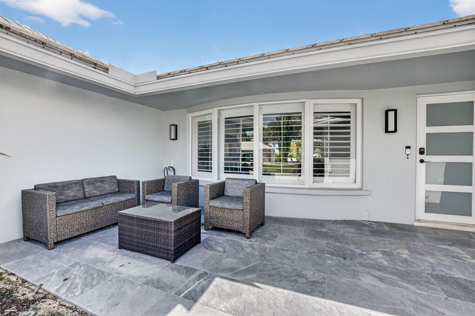 A patio features gray stone flooring, wicker furniture, and a white door with glass panels — 891 Hickory Terrace, Boca Raton FL 33486, BOCA RATON, FL