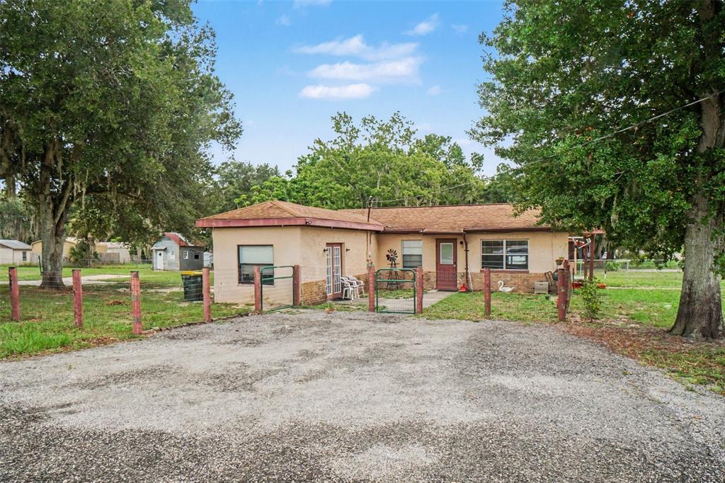 A single-story house with a gravel driveway, fenced yard, and mature trees — 415 LAKE JUNE ROAD, LAKE PLACID, FL