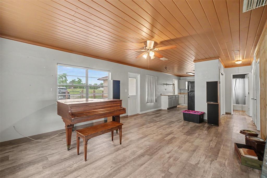 A living room features a wood-paneled ceiling, light-colored walls, wood-look flooring, and a grand piano — 415 LAKE JUNE ROAD, LAKE PLACID, FL