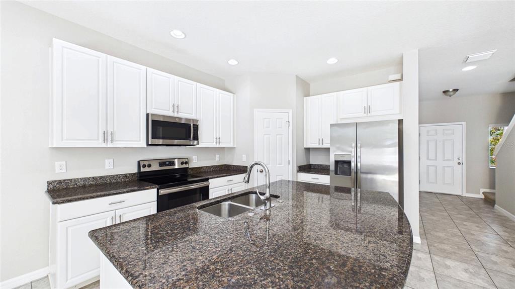 A kitchen features white cabinets, dark granite countertops, stainless steel appliances, and a central island — 7214 GRAND ELM DRIVE, RIVERVIEW, FL