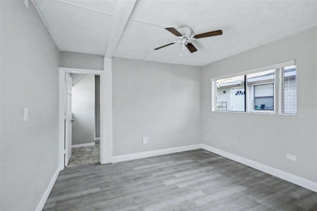 An empty bedroom features light gray walls, wood-look flooring, a ceiling fan, and a window — 2214 QUALITY LIFE CENTER WAY, FORT MYERS, FL