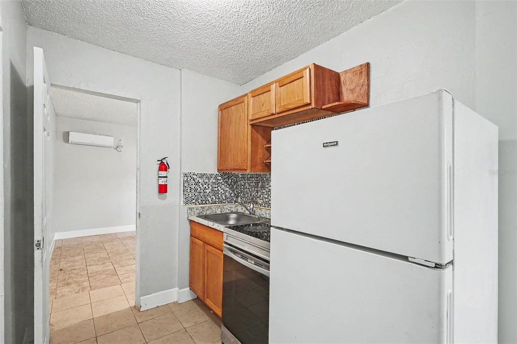 A small kitchen features wooden cabinets, a white refrigerator, and a tiled backsplash — 2214 QUALITY LIFE CENTER WAY, FORT MYERS, FL