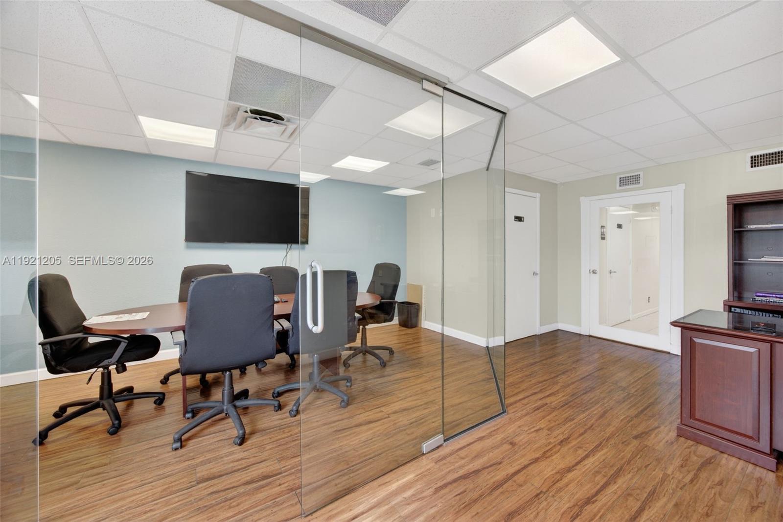 A glass-enclosed conference room features a wooden table, office chairs, and wood-look flooring — 16155 SW 117th Ave # 15, Miami FL 33177, MIAMI, FL