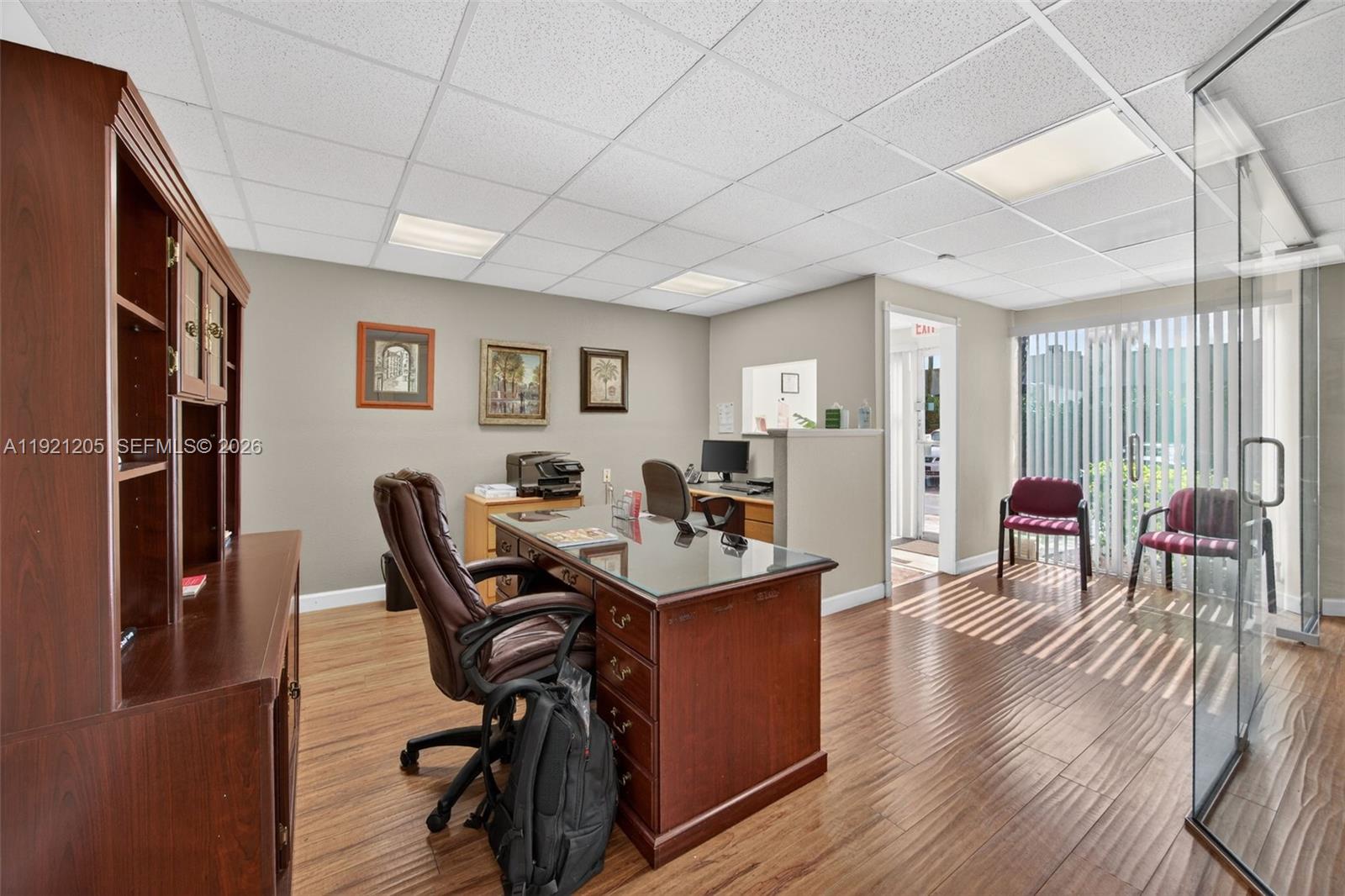 An office space features a wooden desk, leather chair, wood-look flooring, and a glass partition — 16155 SW 117th Ave # 15, Miami FL 33177, MIAMI, FL