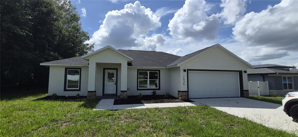 A single-story house with a white stucco exterior, dark trim, and a two-car garage — 7536 SW 129TH PLACE, OCALA, FL