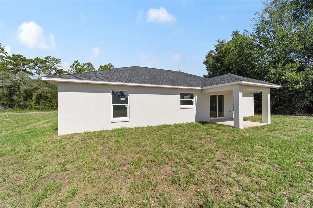 The exterior rear view of a single-story house features a covered patio and lawn — 7536 SW 129TH PLACE, OCALA, FL