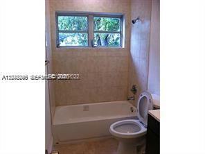 A bathroom features a white bathtub, a toilet, and light-colored tiled walls — 1231 NW 190th St, Miami Gardens FL 33169, MIAMI GARDENS, FL