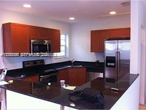 A kitchen features dark wood cabinets, black countertops, and stainless steel appliances — 1231 NW 190th St, Miami Gardens FL 33169, MIAMI GARDENS, FL