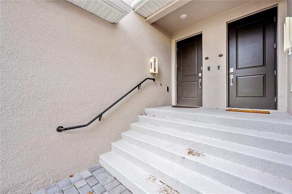 A concrete staircase with a black handrail leads to two dark brown entry doors — 17560 BORACAY COURT UNIT 201, VENICE, FL