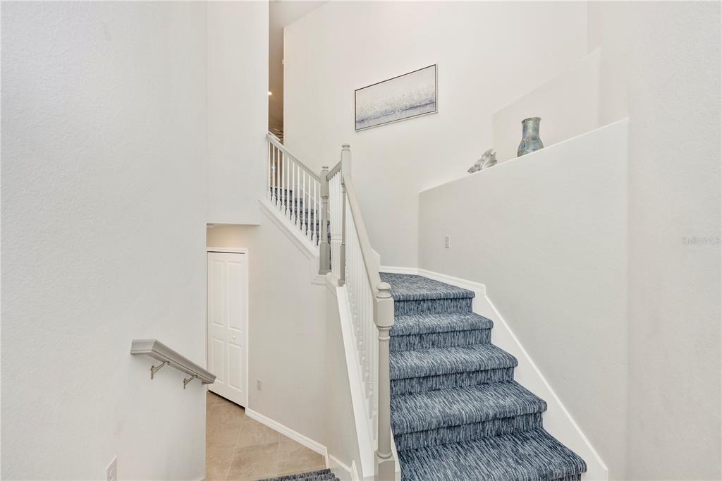 A staircase with blue patterned carpet leads upward past a white wall with decor — 17560 BORACAY COURT UNIT 201, VENICE, FL