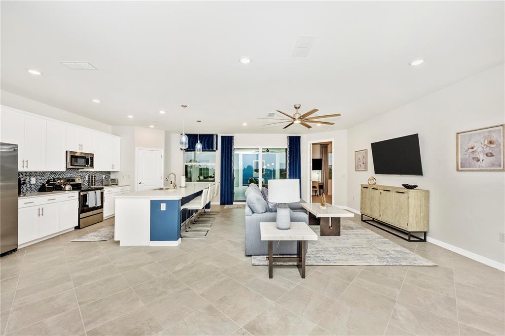 An open-concept kitchen and living area features white cabinetry, a blue island, and tile flooring — 17560 BORACAY COURT UNIT 201, VENICE, FL