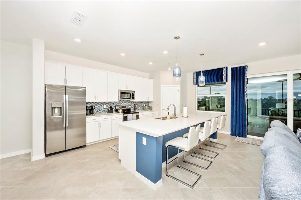 A modern kitchen features white cabinets, a blue island with bar seating, and stainless appliances — 17560 BORACAY COURT UNIT 201, VENICE, FL