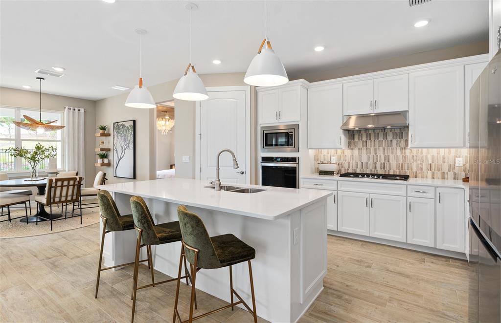 A modern kitchen features white cabinetry, a central island with bar seating, and tile flooring — 5042 DANCY LANE, ST CLOUD, FL